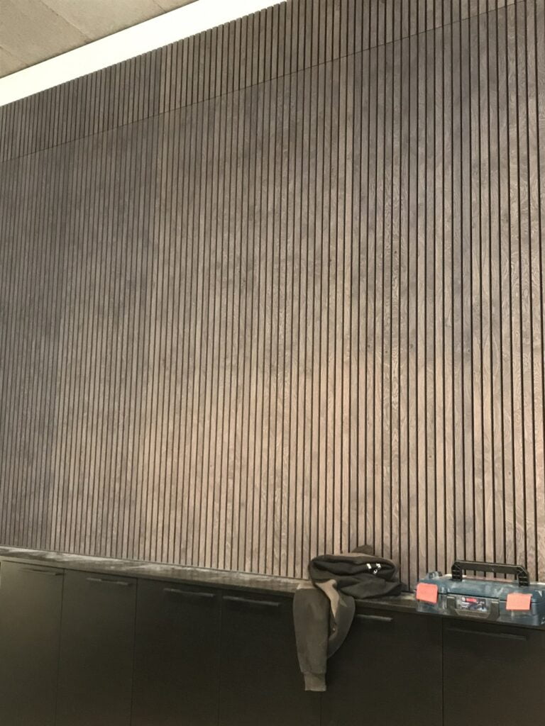 Væg med lodrette træpaneler og sort skab nedenfor