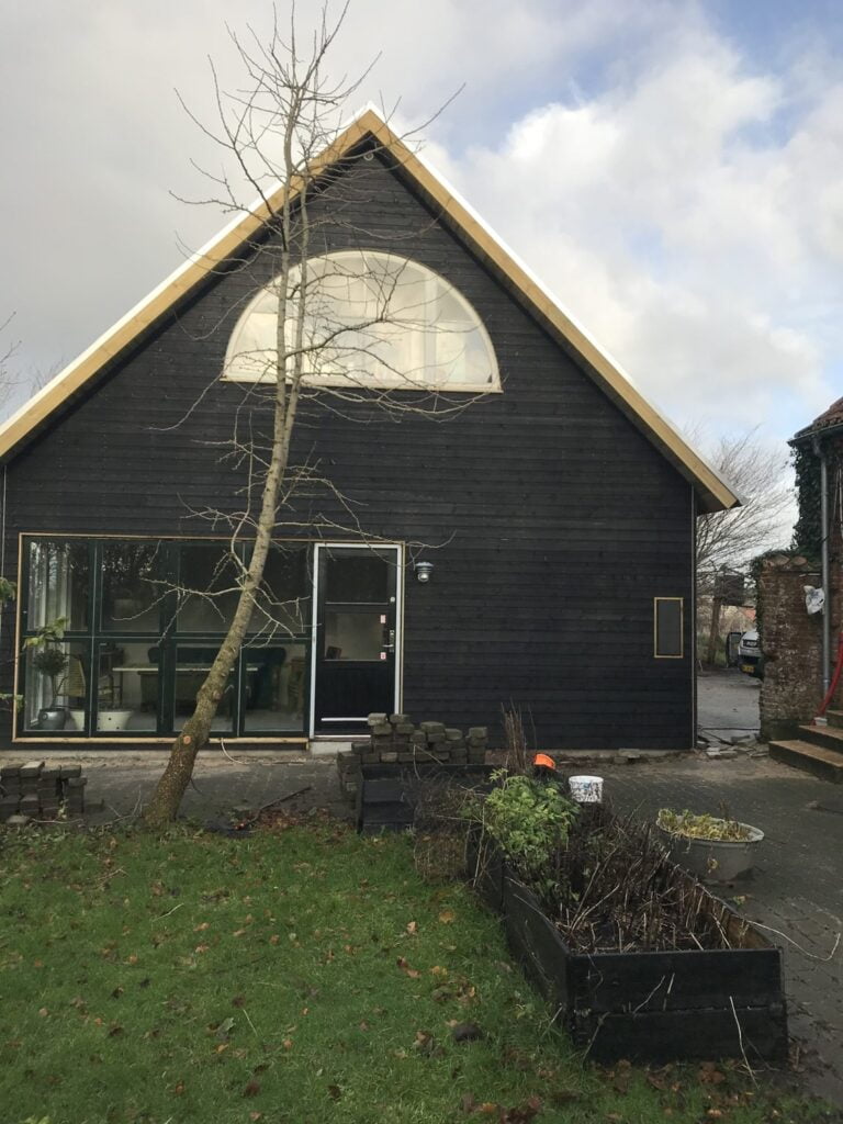 Sort træhus med stor rund vindue og have